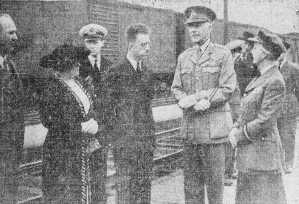 Black and white photograph of Princess Alice and Governor General, the Earl of Athlone. The couple, dressed in military garb, are greeted at the train station in Mont-Joli by city officials. The train cars can be seen in the background.