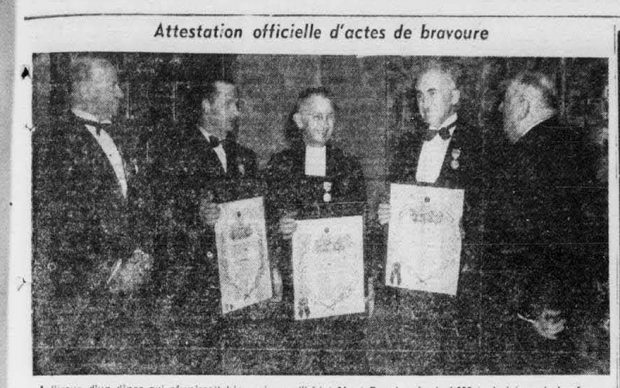 Black and white photograph from a newspaper of five men in black suits. Three men in the middle are holding white certificates. Two men flanking them are empty-handed.