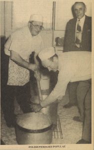 Newspaper clipping of a photograph - a man wearing a short apron and holding a large stick in a large metal pot that another man, dressed the same, is turning on the floor. A man in a suit stands in the background. The caption at the bottom of the image reads Polish Perogies Popular.