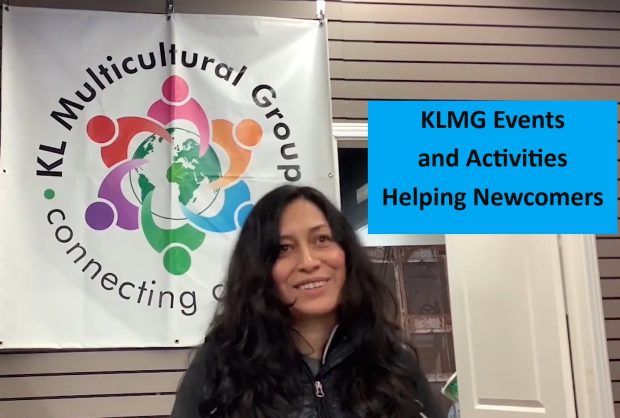 Sandra Reygada Licuime is sitting in front of the Kirkland Lake Multicultural Group sign, facing the camera.