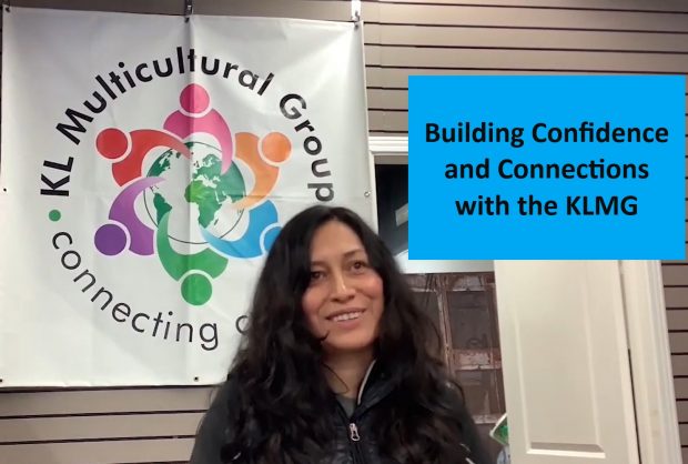 Sandra Reygada Licuime is sitting in front of the Kirkland Lake Multicultural Group sign, facing the camera.