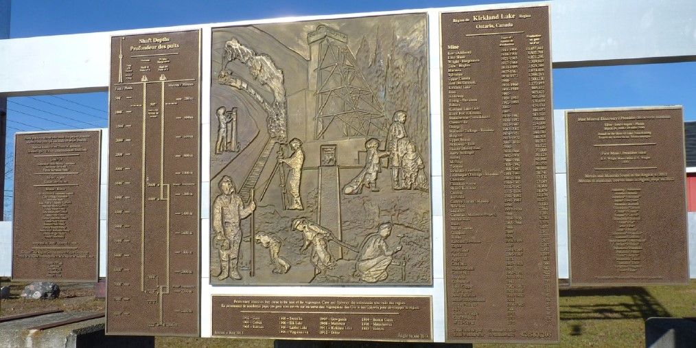 Colour photograph of a large bronze plaque located at the Toburn Mine site in Kirkland Lake. The centre image represents the history of the community.