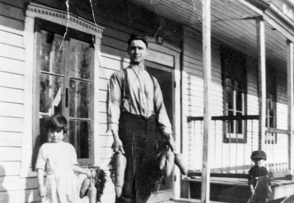 In the centre, Alphonse Mérineau,with his daughter Georgette on the left, in front of their home on Du Pressoir Street. They are holding big carrots. Little Alfred Mérineau is on the right, near the porch, with a cap on his head.