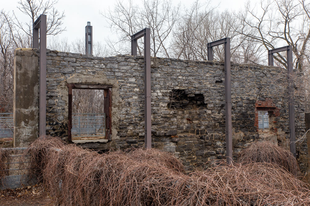 On the mills’ dike, a restored masonry wall is encircled with four steel structures. Each represents the volume of previous industrial buildings. Behind the wall, the steel tower occupies the place where the factory’s tall smokestack once stood.