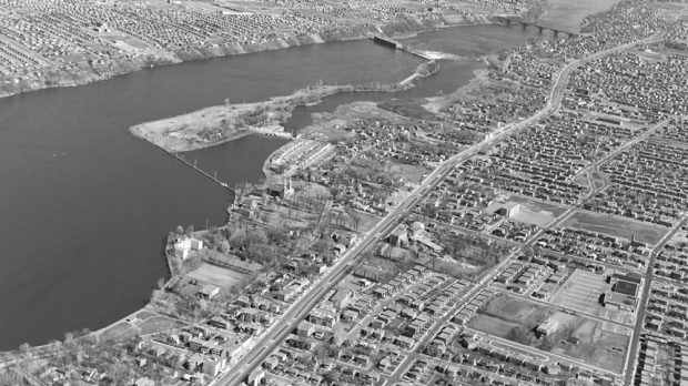Oblique aerial view of the Des Prairies River in 1963. In the foreground, the newer, heavily populated residential neighbourhoods of Sault-au-Récollet. On the river, La Visitation Island, the hydroelectric power plant and, in the top right corner, the Pie-IX bridge in Montréal-Nord.