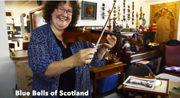 A smiling woman holding a violin from the 1800s.