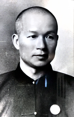 Black and white head and shoulders portrait photograph of a youngish Chinese man with very closely cropped hair, clean shaven, wearing a dark colored Chinese-style collarless jacket.