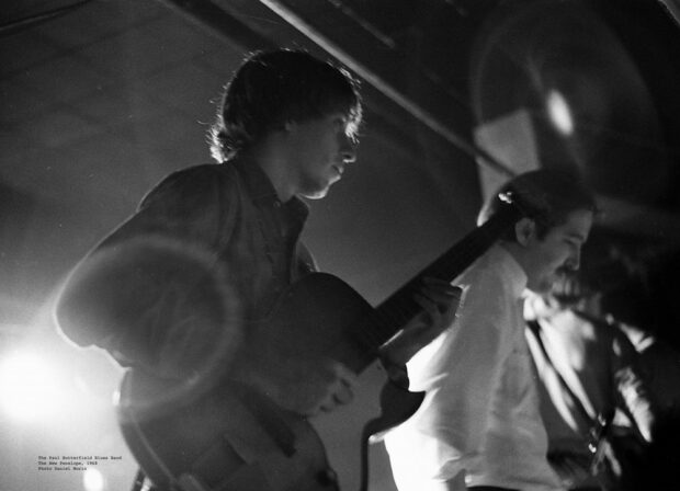 Two members of the Paul Butterfield Blues Band are seen in a black and white photograph taken from up close on the side of the stage.