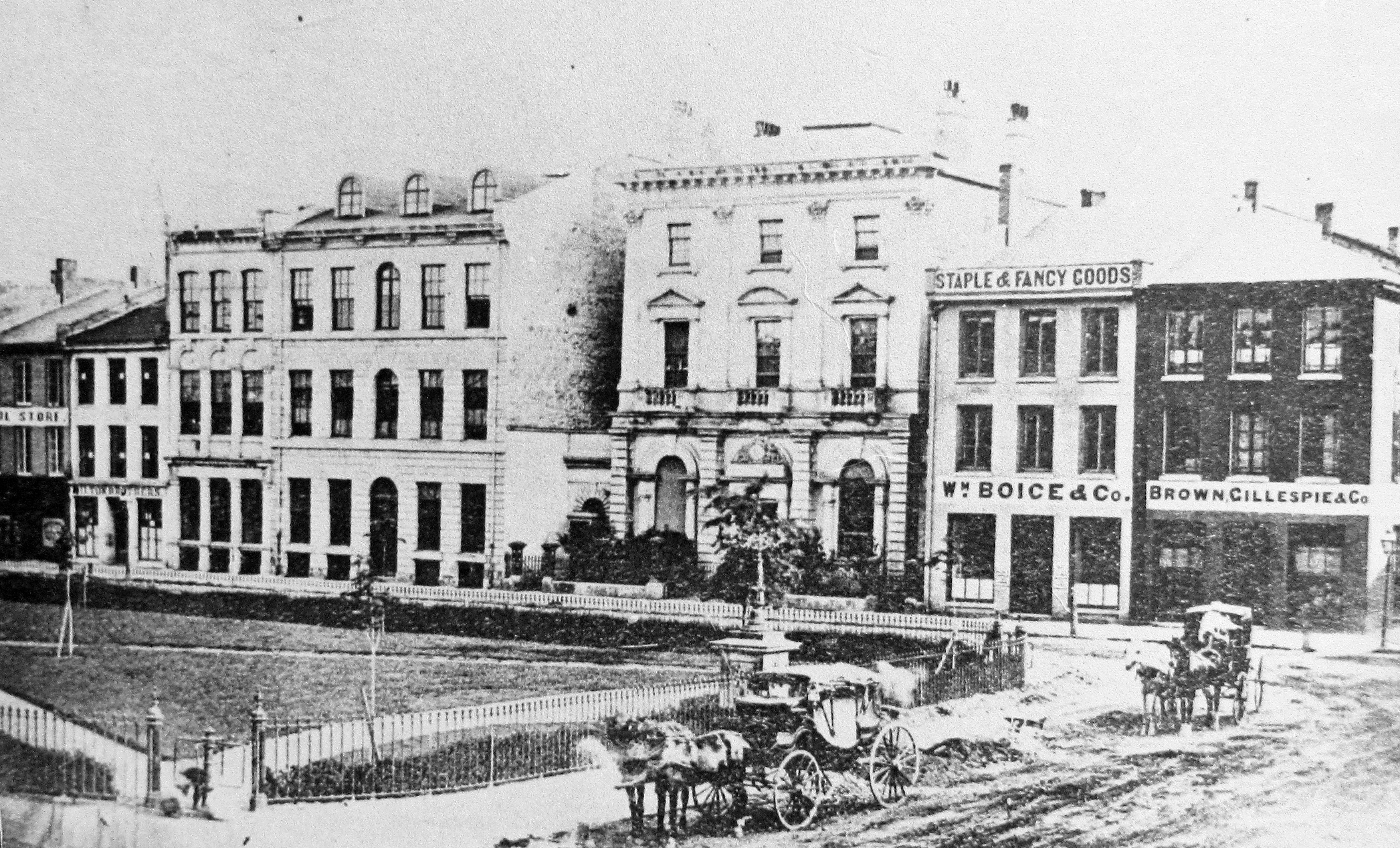 Small shops line one street over looking Gore Park, while horse drawn carriages drive down the cross-street.