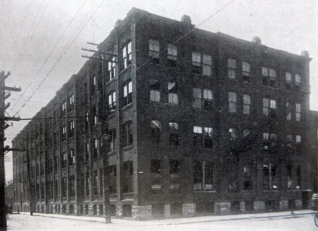 Photographie de l’usine de quatre étages de John McPherson, occupant près d’un pâté de maisons complet.