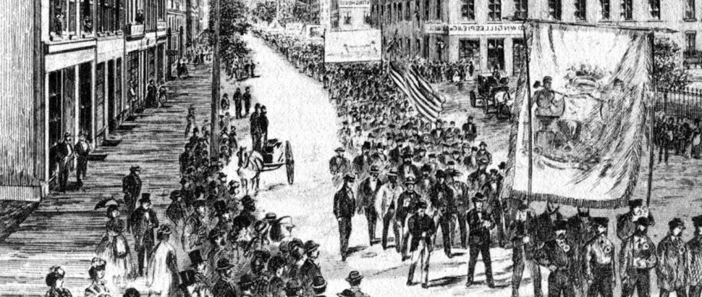 A cropped version of the cover of the Canadian Illustrated News from June 8 1872 depicts the parade of workers on May 15th 1872. There are dozens of spectators watching from the sidewalks as the parade of workers carry large banners and flags through the centre of the street.