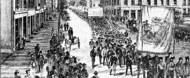 A cropped version of the cover of the Canadian Illustrated News from June 8 1872 depicts the parade of workers on May 15th 1872. There are dozens of spectators watching from the sidewalks as the parade of workers carry large banners and flags through the centre of the street.