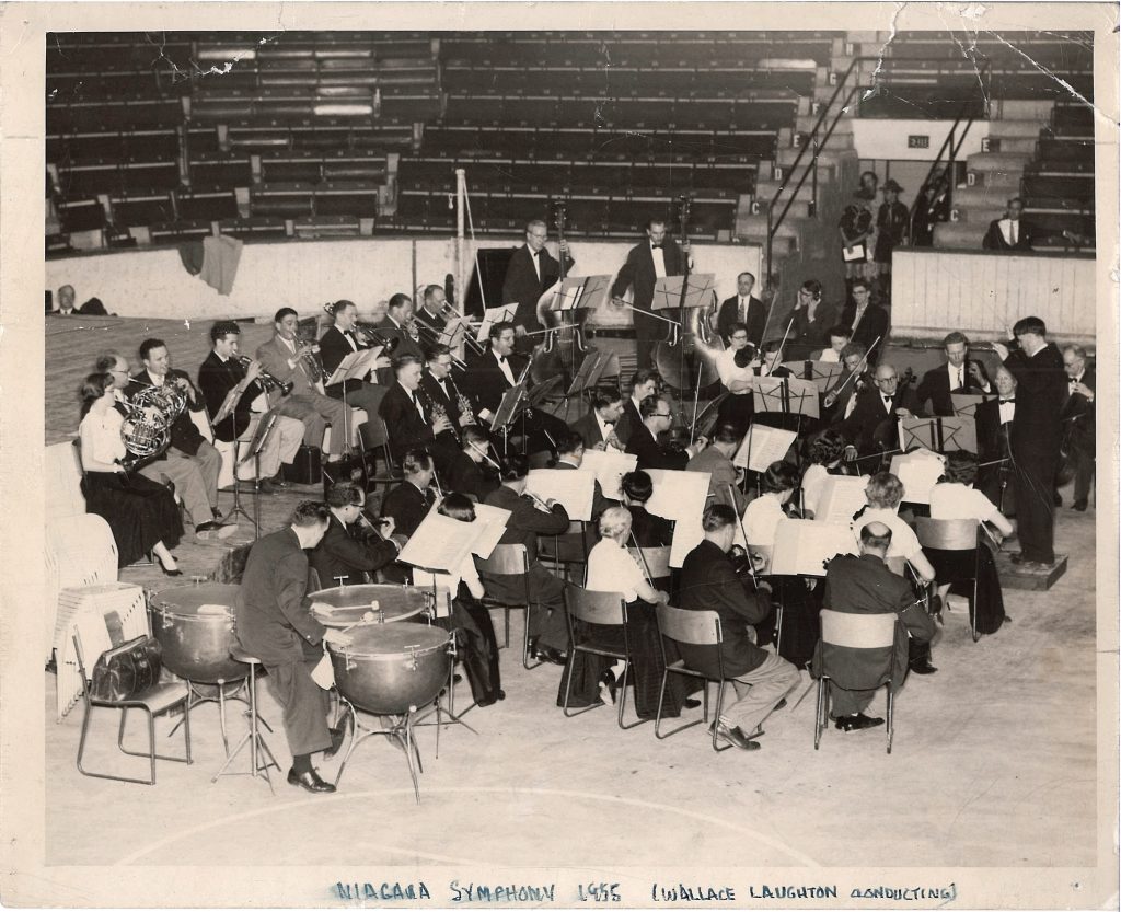 Wallace Laughton conducts the orchestra in a stadium