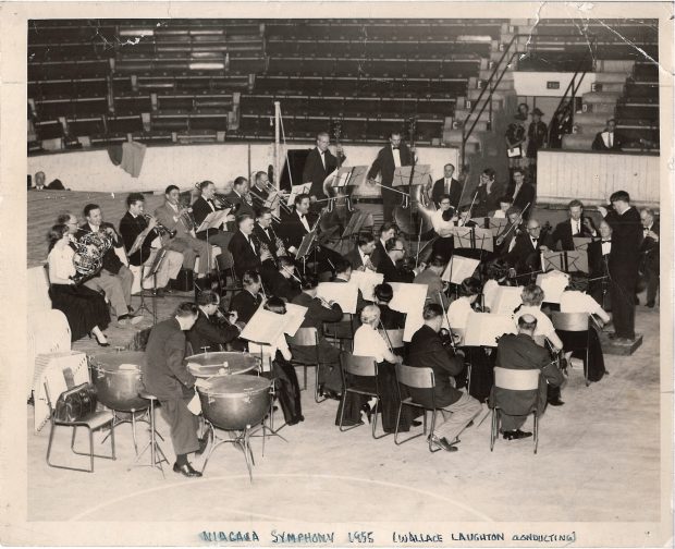 Wallace Laughton conducts the orchestra in a stadium