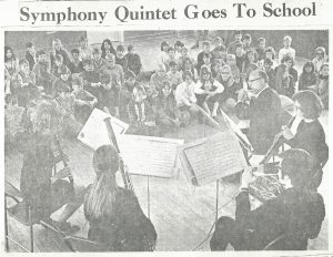 Un quintette de bois joue de la musique pour des étudiants. L’article du journal est « Le quintette de l’orchestre va à l’école. »