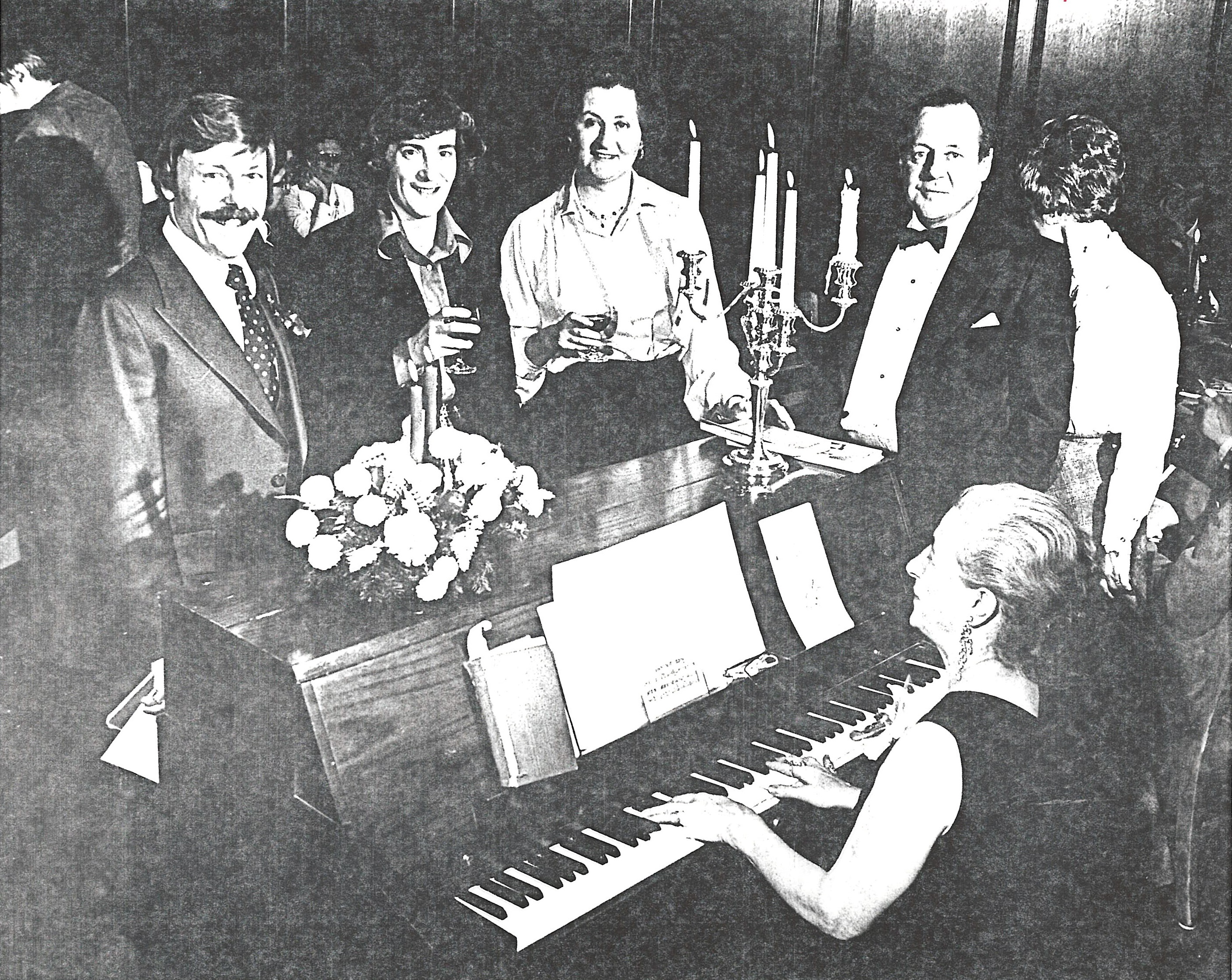 4 board members stand at piano during party