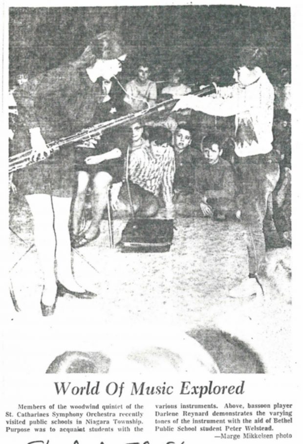 Student looks into bassoon during demonstration. Newspaper article titled “World of Music Explored”