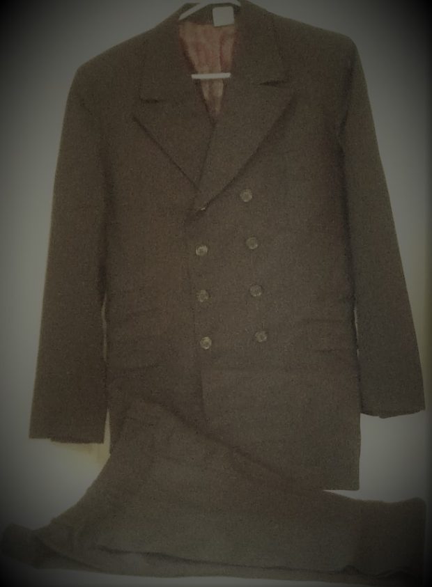 Man's two-piece suit - brownish / green faintly patterned cloth - jacket has three buttons on front, three buttons on cuffs, outside pockets with flaps, breast pocket on left side, inside pockets, lined with brown satin in body with striped lining for sleeves - pants have slash side pockets and cuffs at hem.