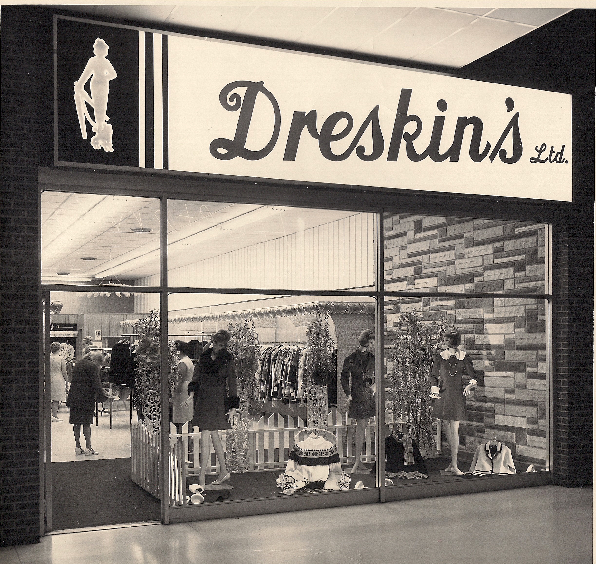 Storefront for shopping mall location of Dreskin’s Ltd. Three mannequins in short coats are arranged in the glass window with racks of clothing and customers seen inside the store.