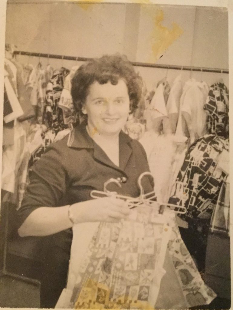 Woman holding bags and hangers – clothing hung on racks behind her.