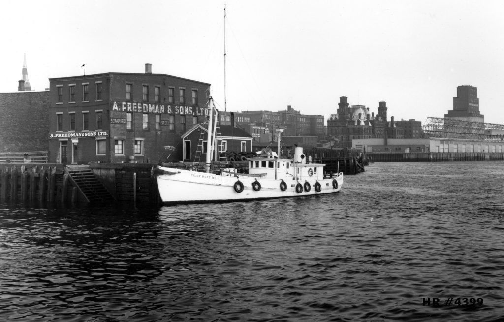 Pilot boat docked at wharf in front of three-storey warehouse for A. Freedman and Sons, Ltd.