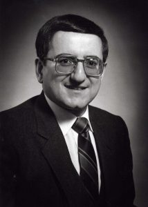 Head and shoulders portrait of man with dark hair and glasses.
