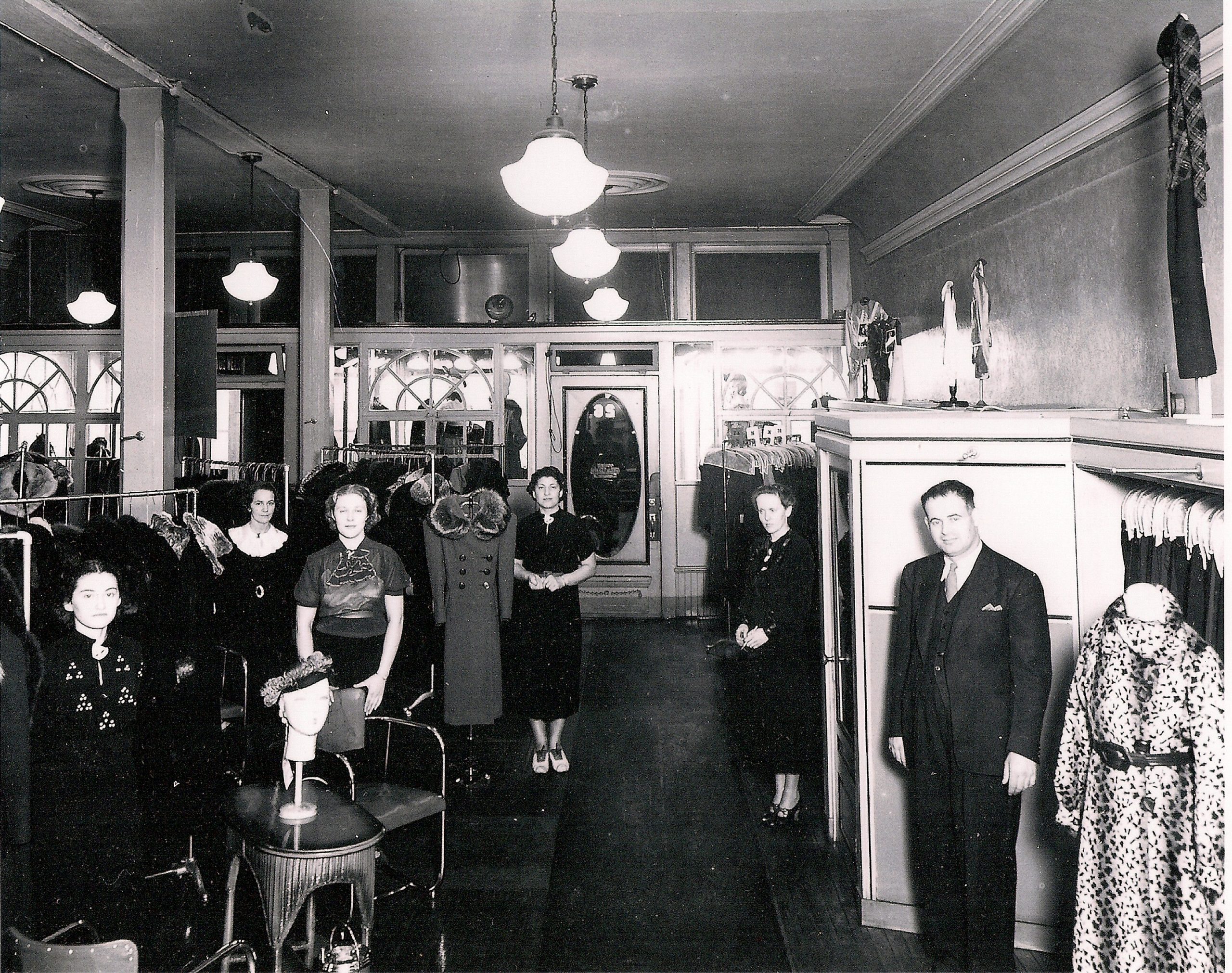 Interior of a ladies' wear store with four female sales clerks and one man. Dresses and coats on racks are to the left.