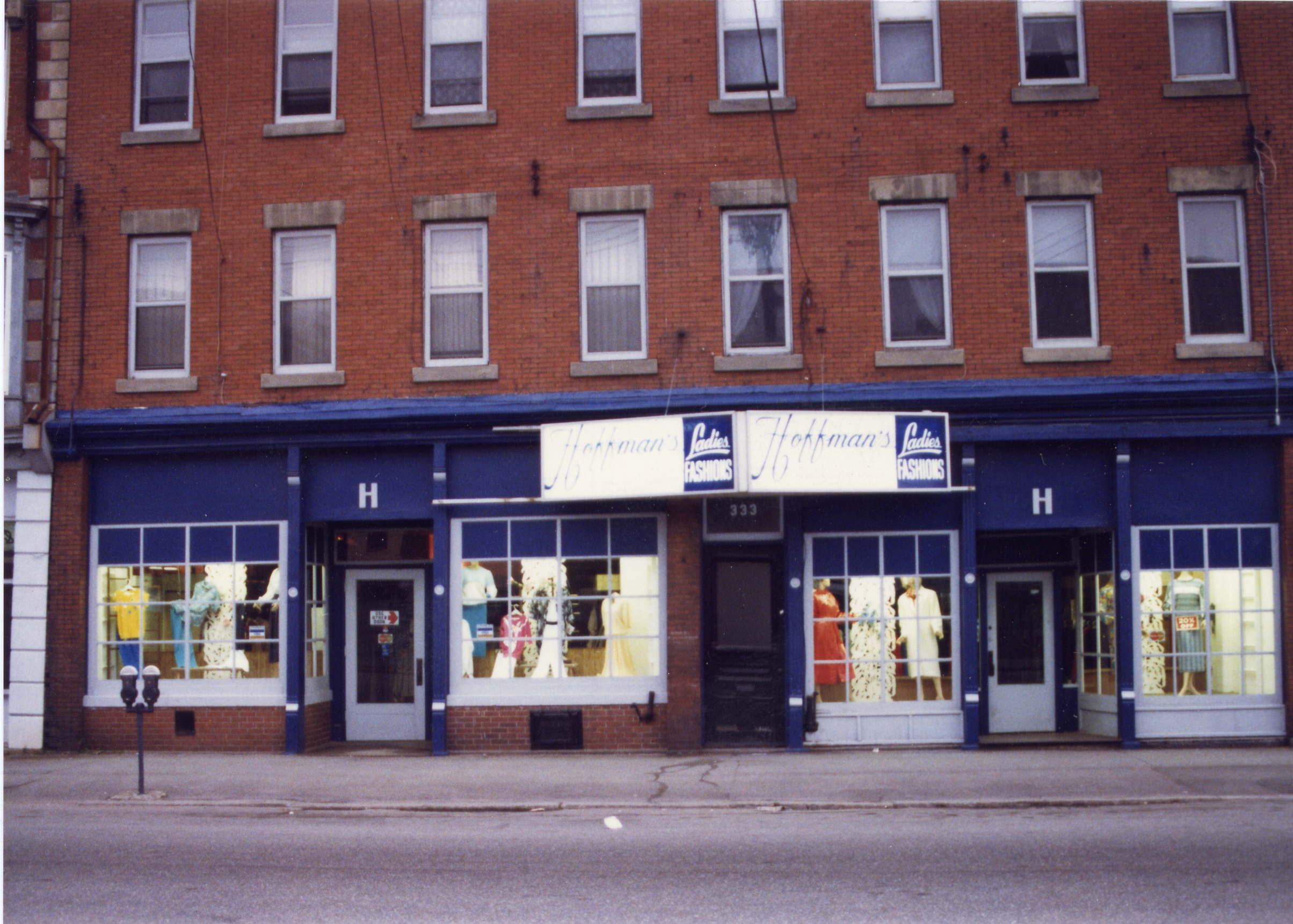Exterior of brick building with store at street level. The store had four display windows with a sign for Hoffman’s centred above the windows.