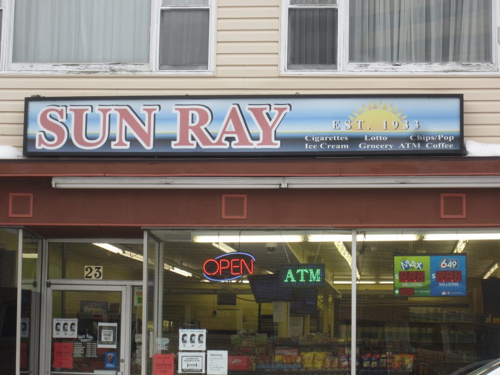 Entrance to Sun Ray convenience store with two large glass windows and doorway.
