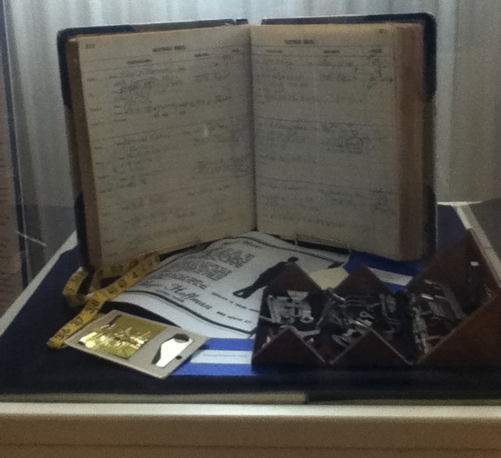 Museum exhibit with handwritten ledger book and small case of sewing machine parts.