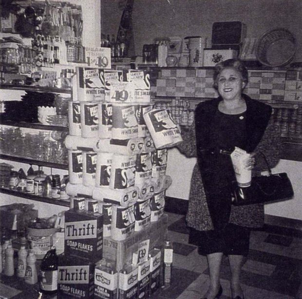 Woman in grocery store holding a carton and a package. Shelves to her left filled with grocery products.