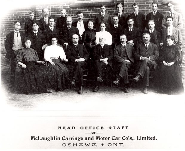 Black and white image of several dozen male and female office workers in formal 1900s clothing posed in front of a brick wall. Caption reads HEAD OFFICE STAFF OF McLaughlin Carriage and Motor Car Co's., Limited, OSHAWA, + ONT