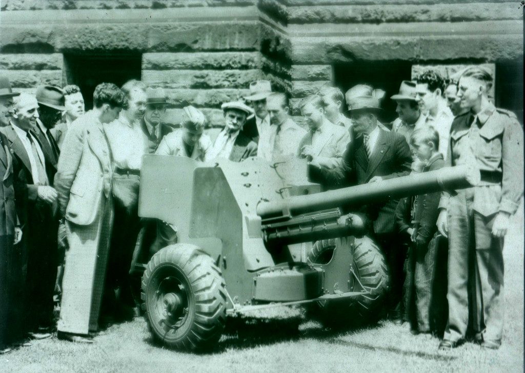 Black and white image of a crowd of men, women and children examining an artillery piece.