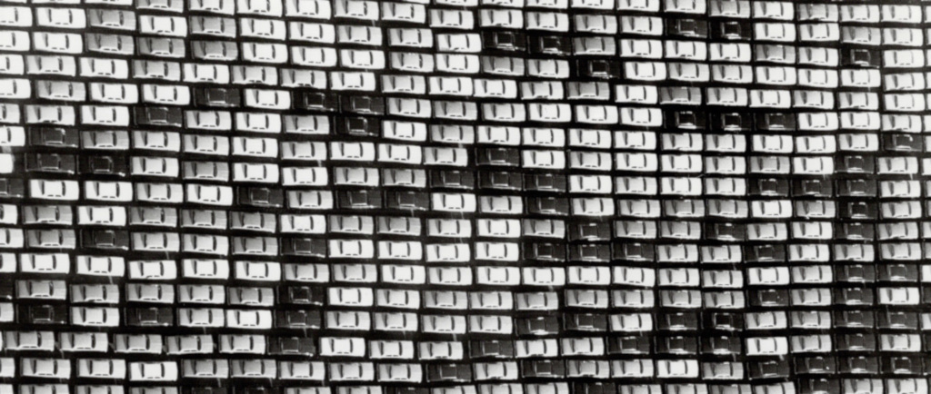 Black and white image of several hundred cars in rows, seen from above.