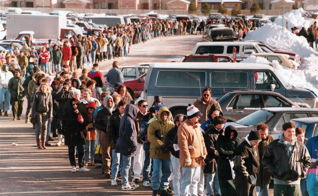 Colour image of several hundred people in winter clothing waiting in line in a snowy parking lot.