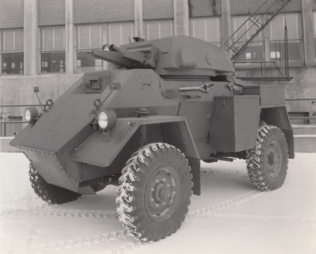 Black and white photograph of an armoured car in front of a factory in the snow