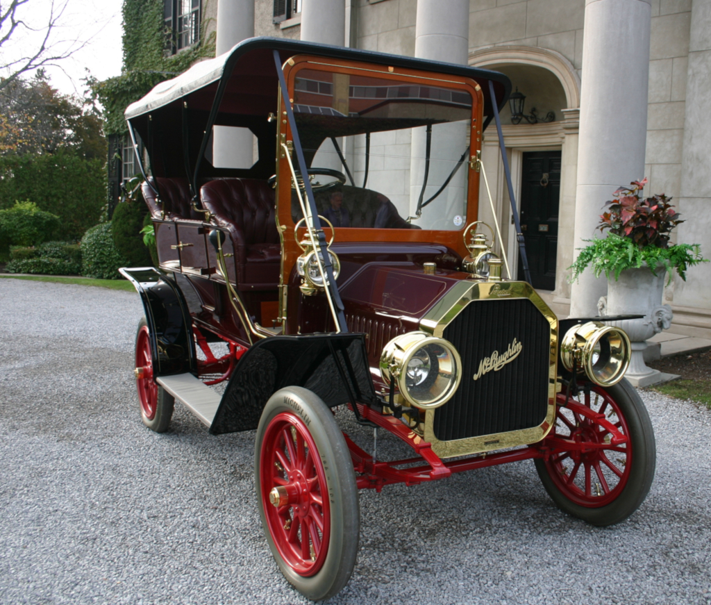 Colour image of an antique automobile parked on a gravel driveway in front of a large marble house.