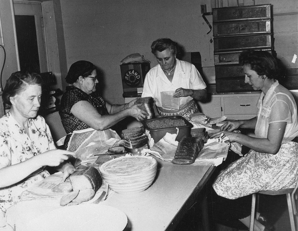 Image en noir et blanc représentant quatre femmes en train de préparer des sandwichs dans une cuisine industrielle.