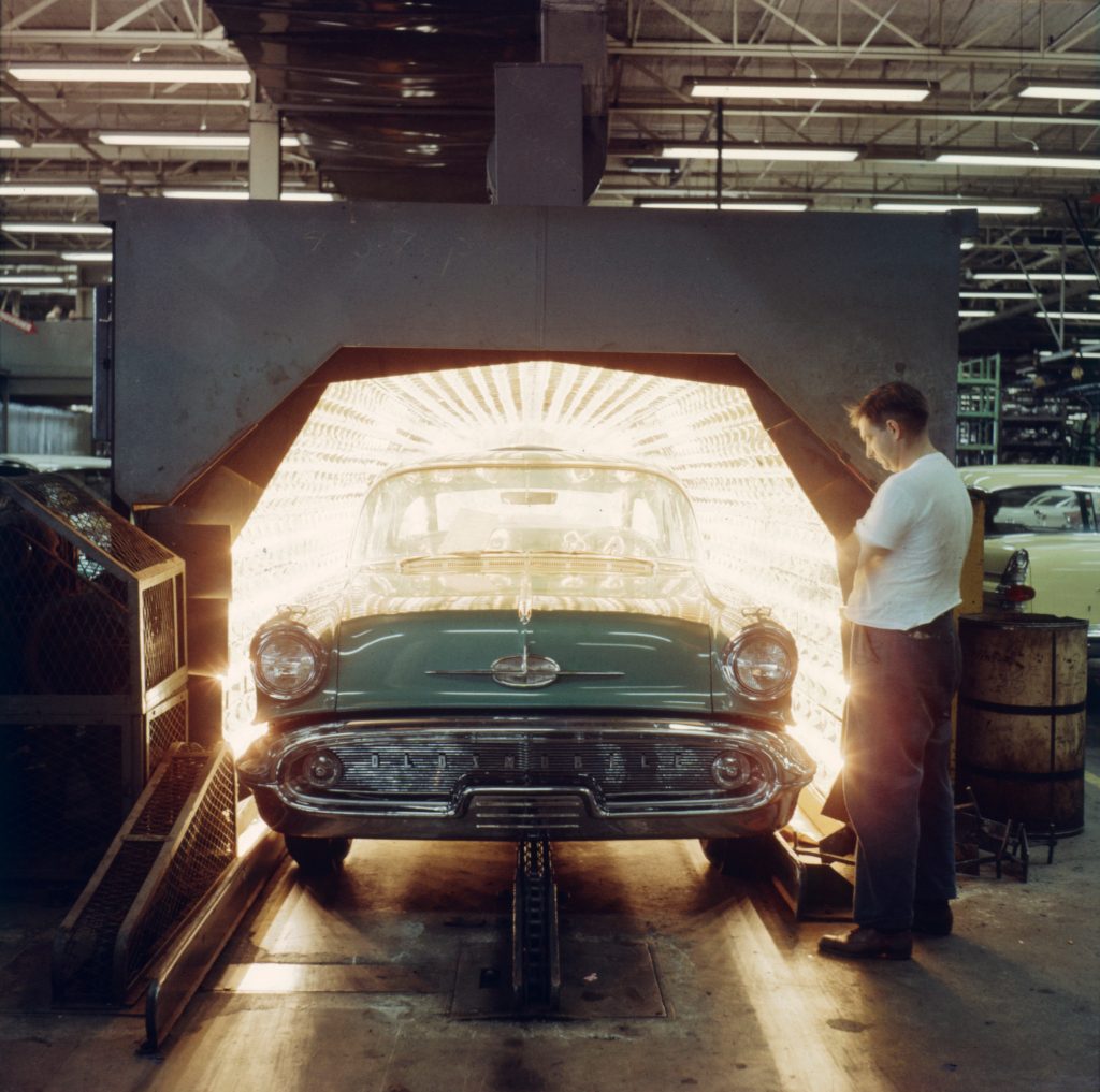 A man watches as a 1950s automobile passes through a large industrial oven.