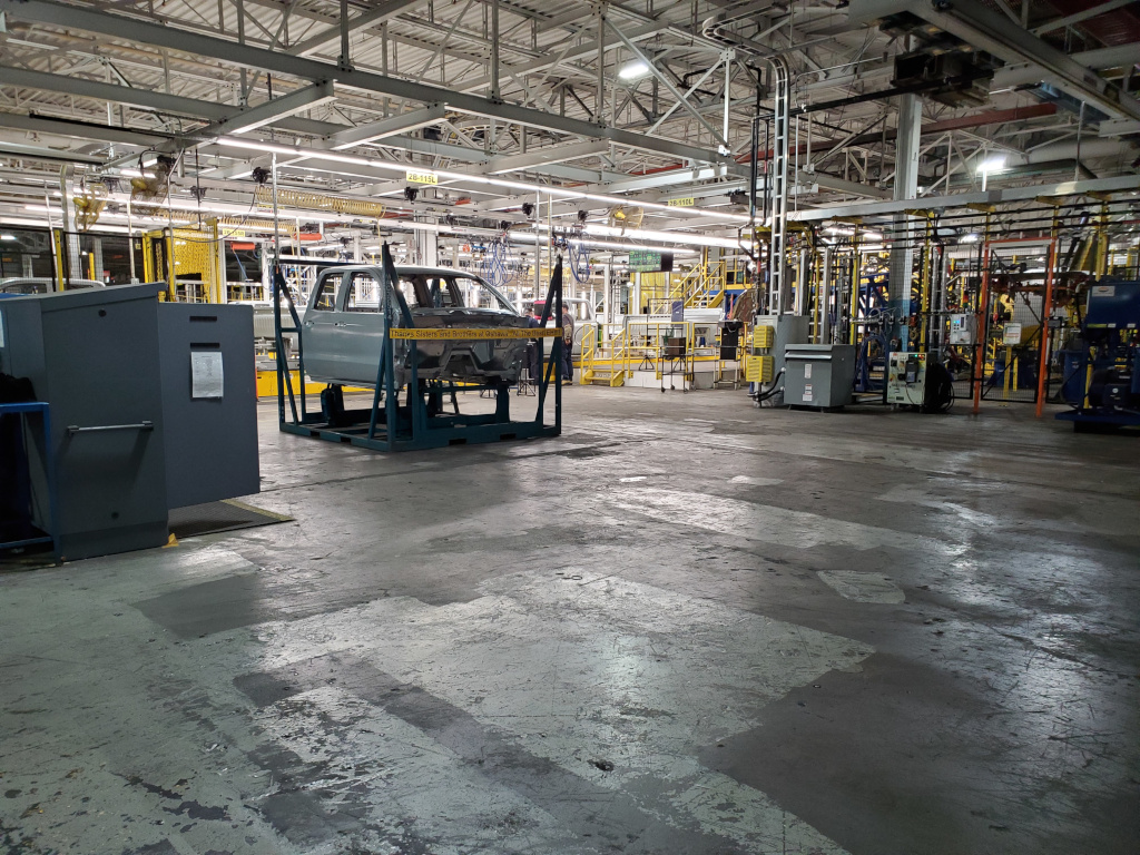 Colour image of a partially-assembled truck cab sitting alone on a pallet in an empty factory space.