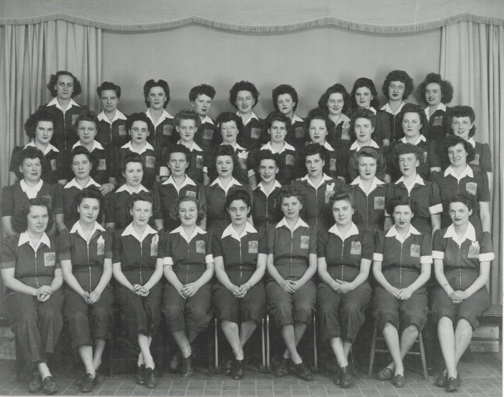 Forty women in one-piece jumpsuits pose for a group photo.