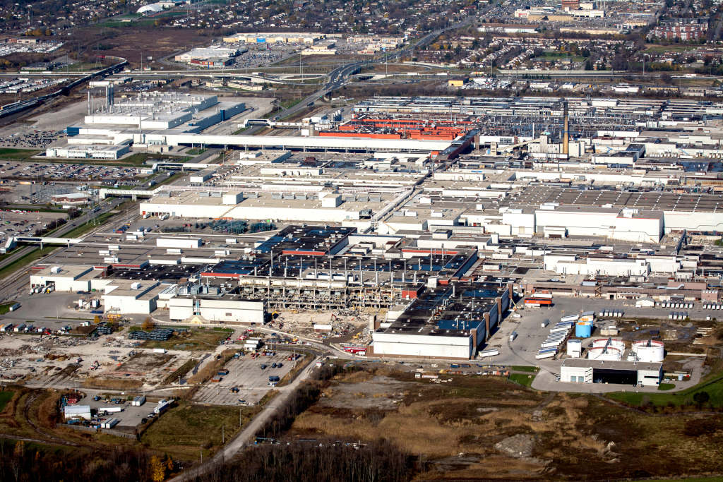 Aerial photograph of a series of large industrial buildings and parking lots next to a highway interchange.