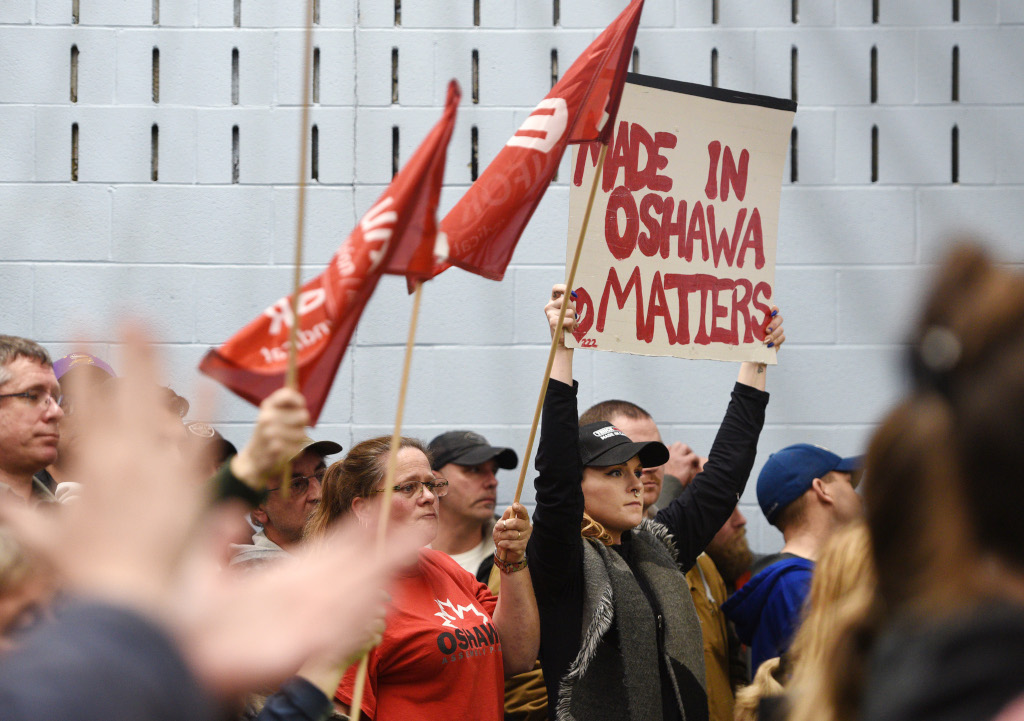 Plusieurs dizaines de manifestants tiennent des drapeaux et une pancarte. Sur la pancarte on peut lire SI C’EST FABRIQUÉ À OSHAWA, ÇA COMPTE.