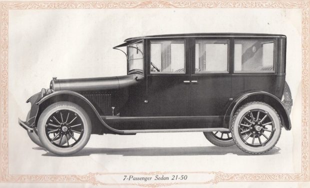 A black and white painting of an automobile. The vehicle has a square top, running boards on the side, and white tires. The caption reads 7-passenger Sedan 21-60.