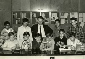 Graham Beard in the middle of two rows of students that are posing with scientific equipment. 1965