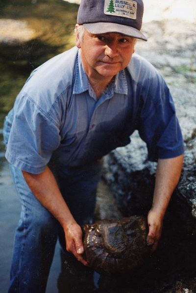 Graham Beard standing in the Englishman River, looking off-camera as he holds a newly unearthed ammonite fossil. c. 2005