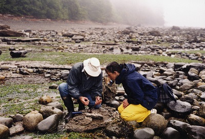 Graham Beard and another amateur paleontologist crouched next to each other, looking at a rock between them that has been cracked open.