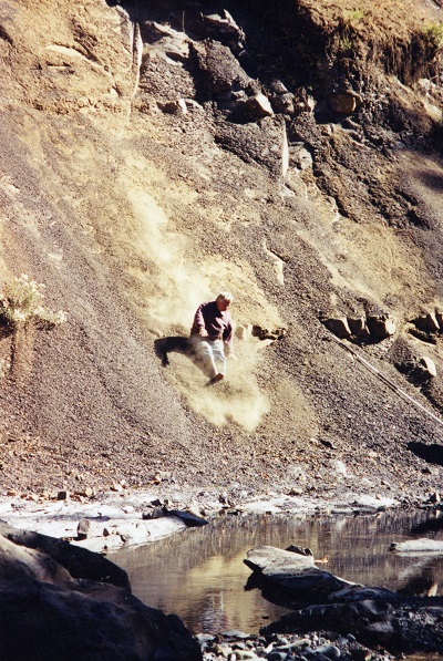 Graham Beard sliding down the bank of a river.