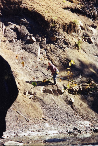 Graham Beard standing on steep riverbank in a fossil-bearing rock formation in the Comox Valley.