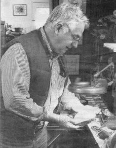 Graham Beard standing in his home, looking at a fossil under lamplight. c. 1995